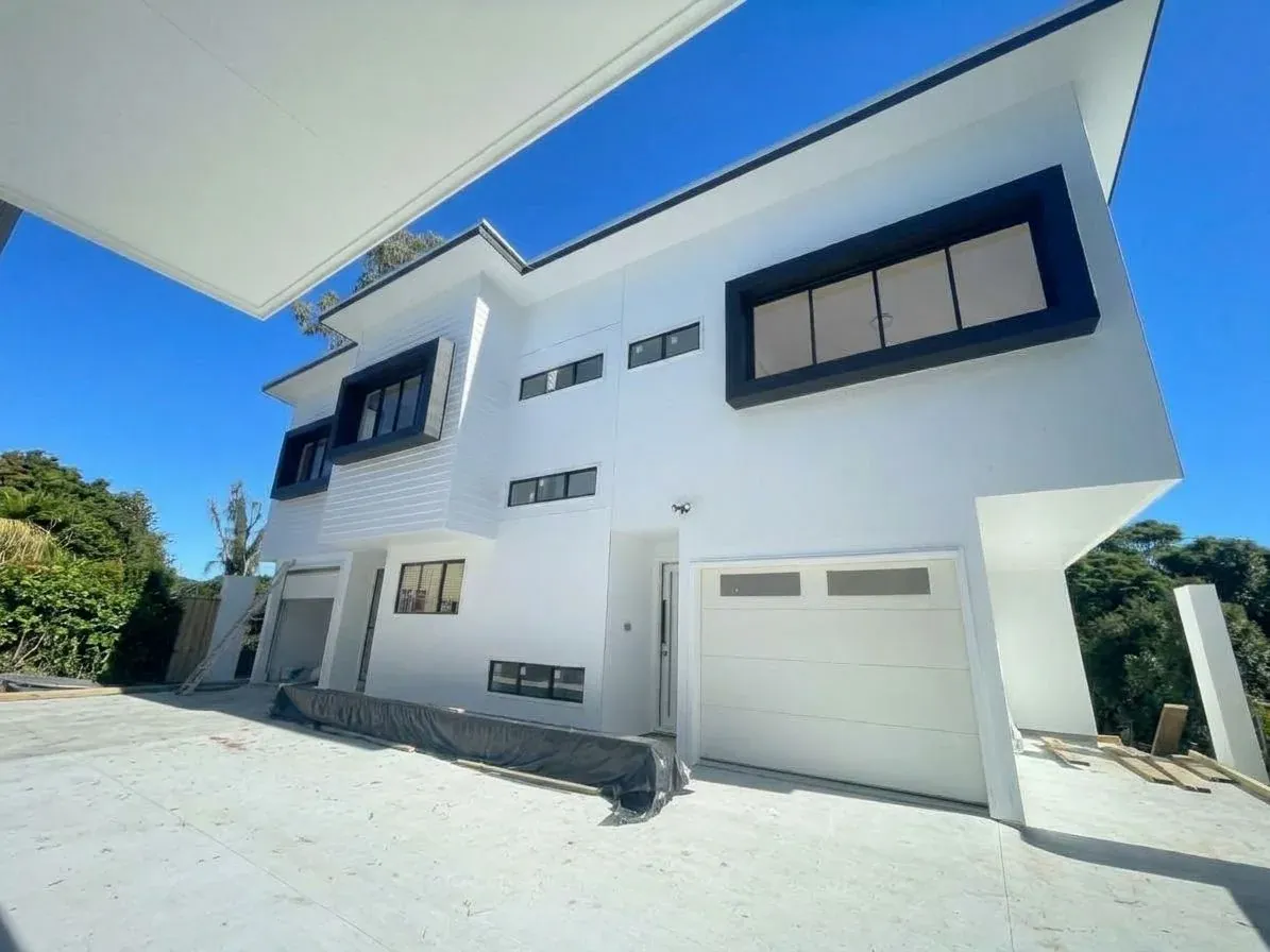 A white two-storey duplex in Coorparoo, Brisbane, with black window surrounds and a single garage under a clear blue sky, freshly painted by AnB
