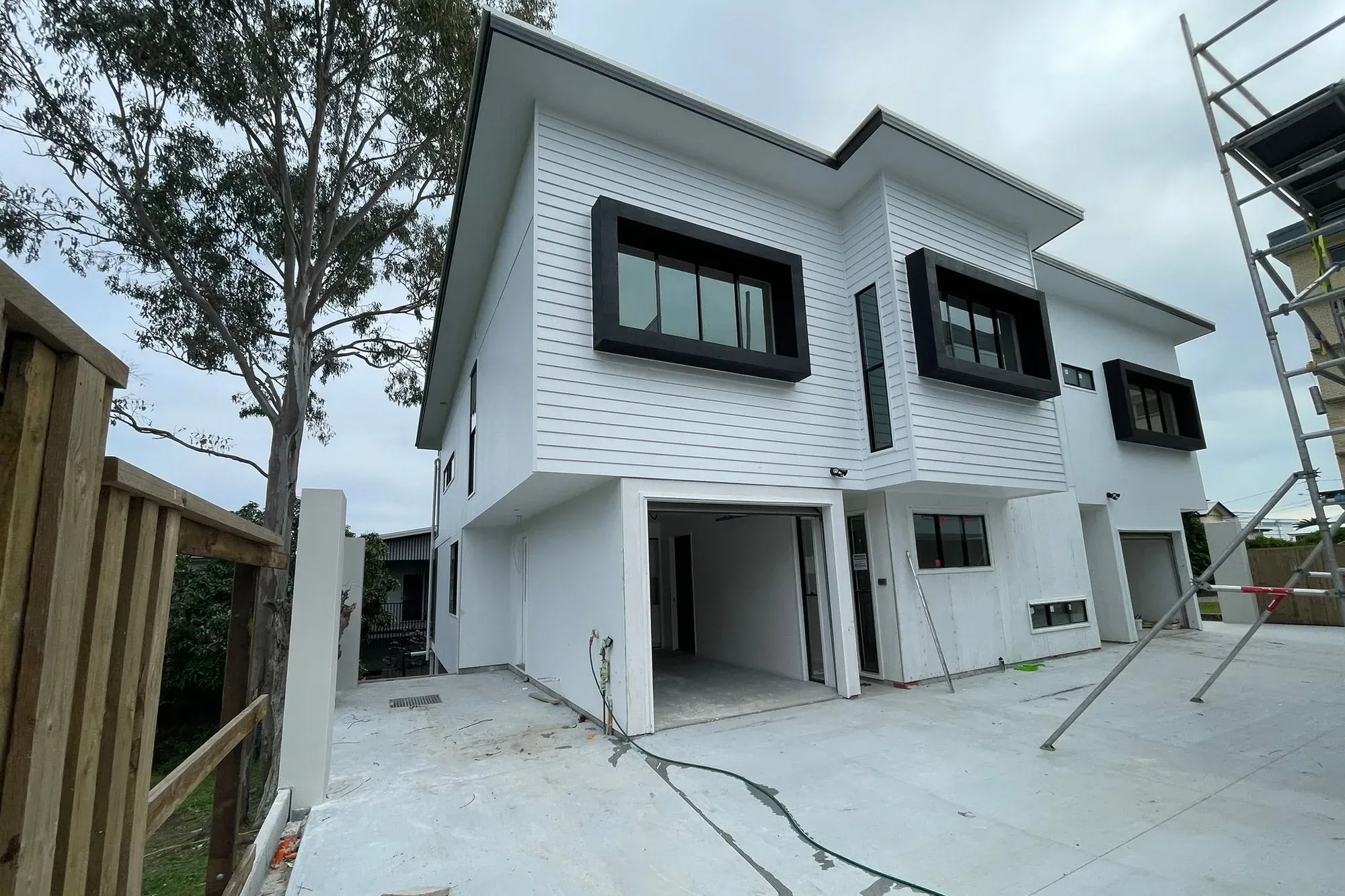 A new-build two-storey home in Coorparoo, Brisbane, with freshly painted white weatherboards and black window surrounds, with scaffolding still up
