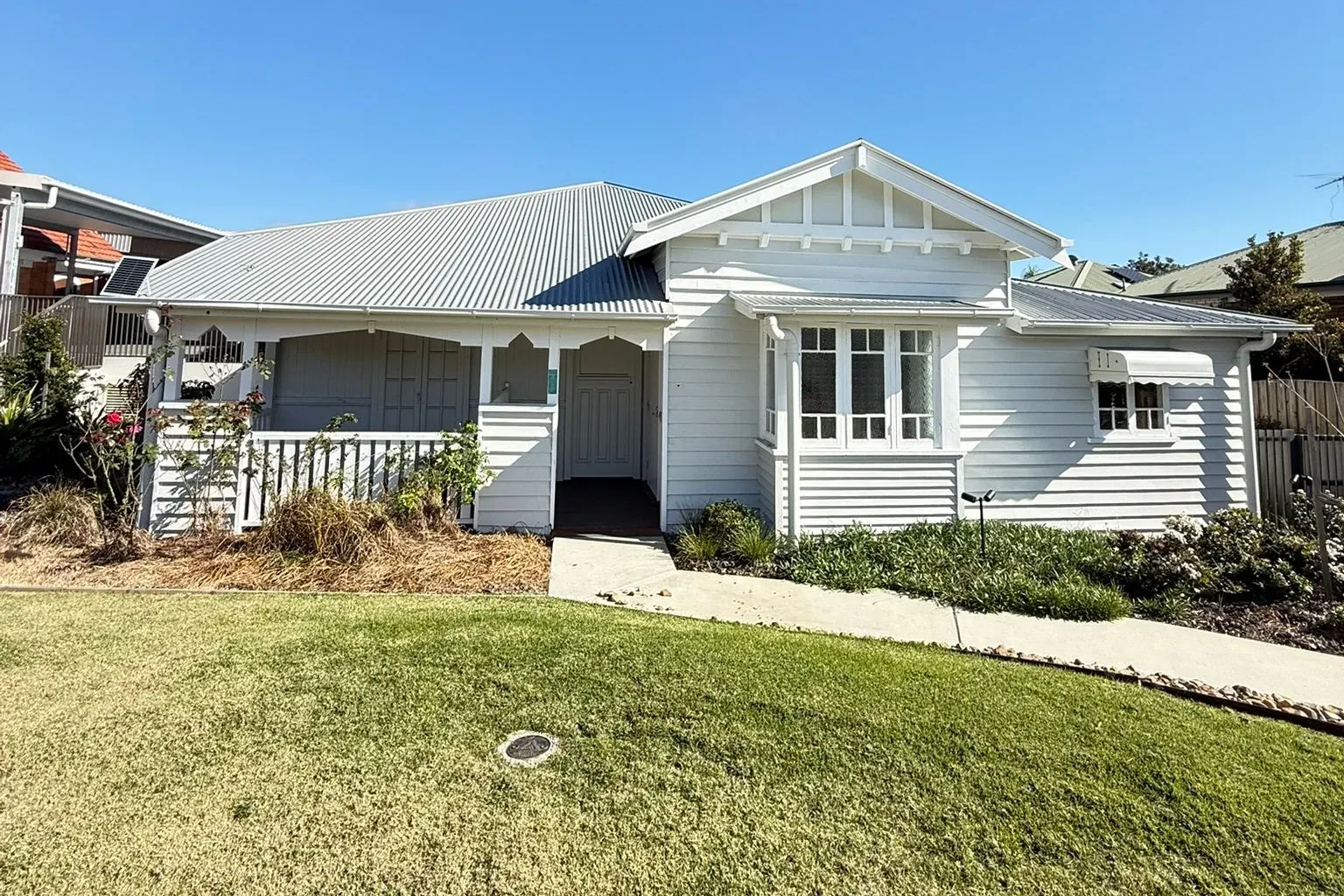 The same Queenslander home after repainting, with crisp white weatherboards and a tidy lawn