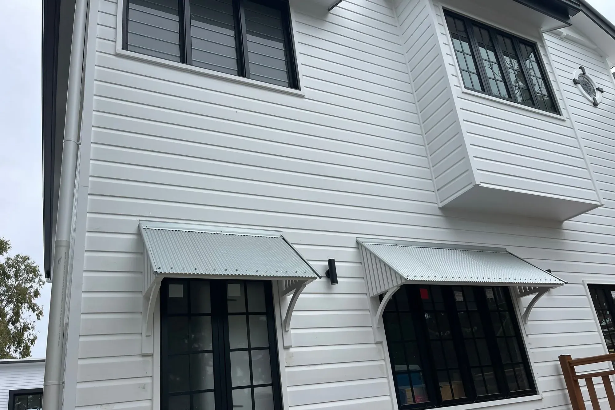 Close view of white painted weatherboards in Coorparoo, Brisbane, with black-framed windows and white corrugated awnings on curved brackets